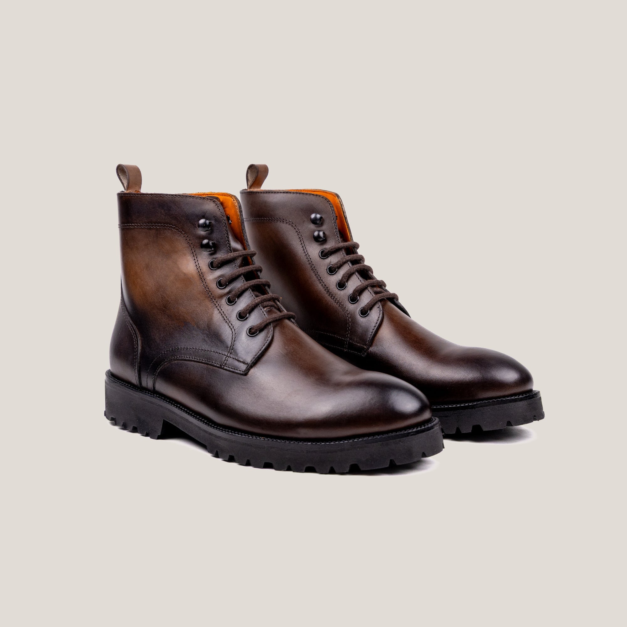 A pair of brown patina leather boots with lace-up closure and rubber soles.